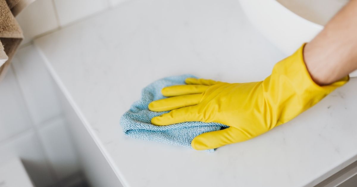 gloved hand wiping bathroom counter with microfiber cloth